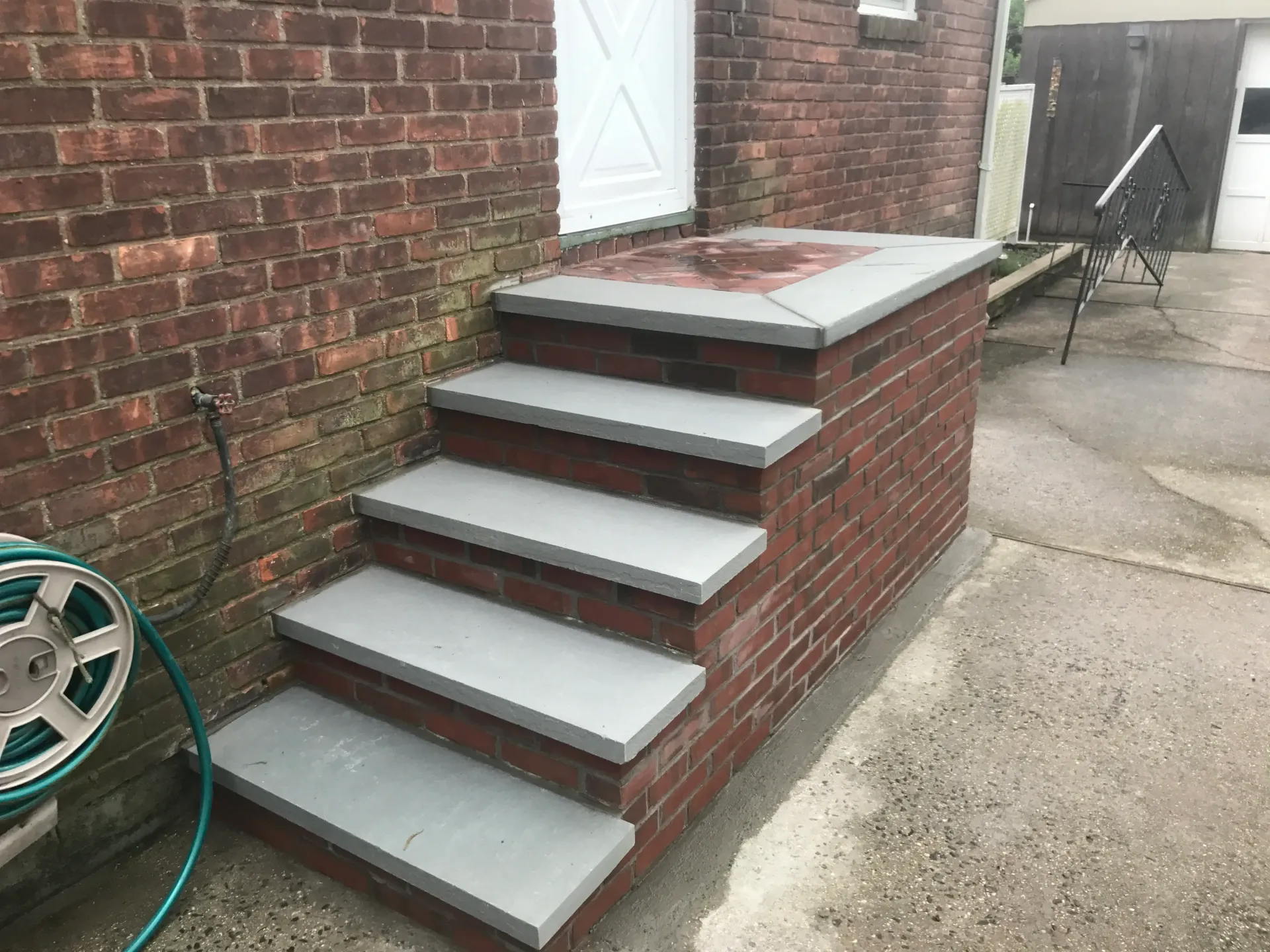 Brick steps with gray treads lead up to a white door on a brick building.