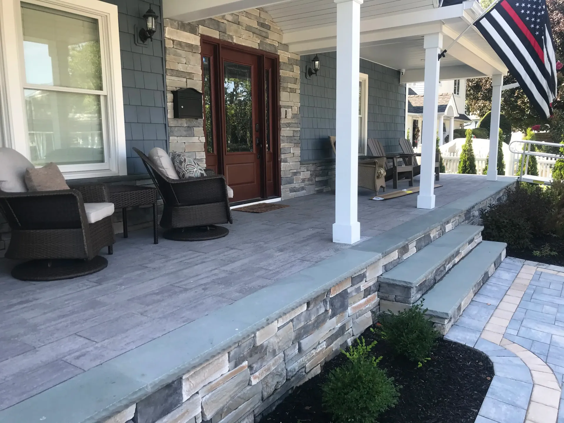 Front porch with stone and wood details, featuring seating and a flag.