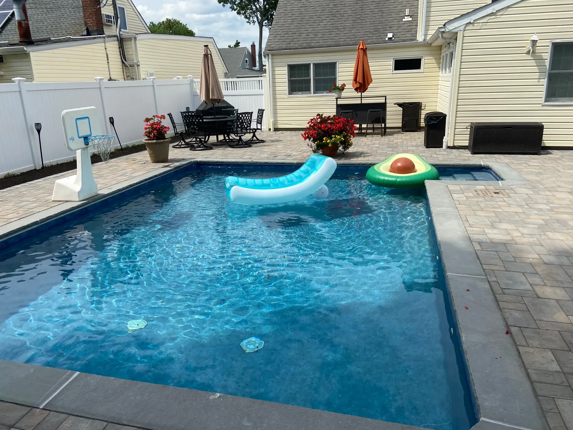 Backyard pool with blue water, floats, and a paved patio.