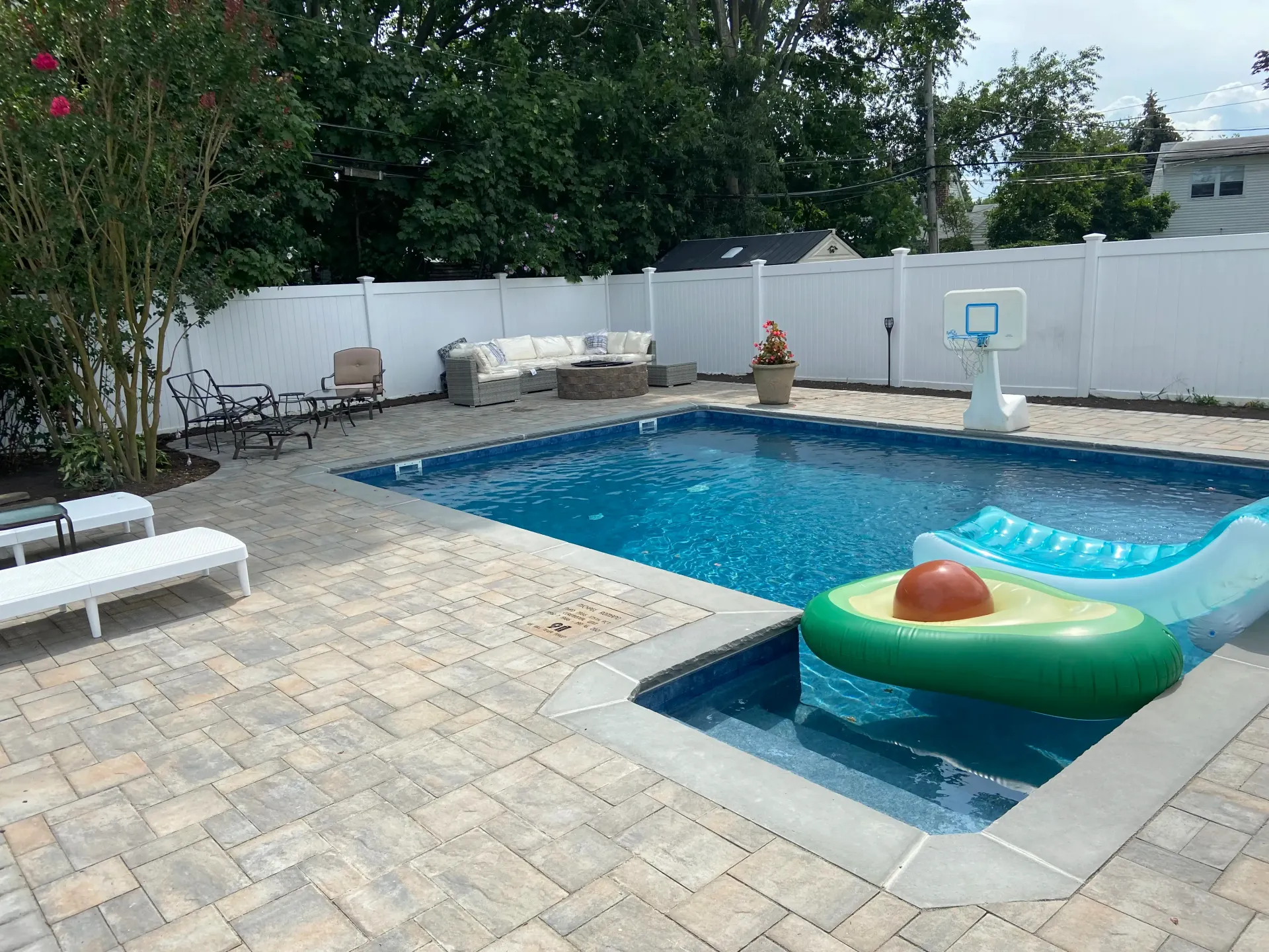 Backyard with a blue pool, avocado float, lounge chairs, and white fence.