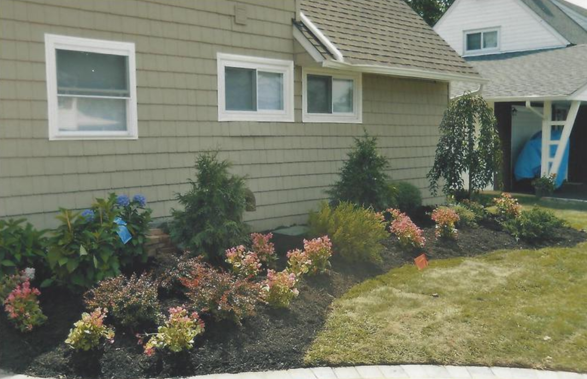 Beige house with a landscaped garden bed of shrubs and colorful flowers.