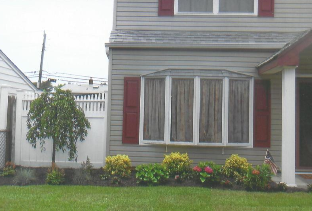 House exterior with a bay window, red shutters, and small garden.