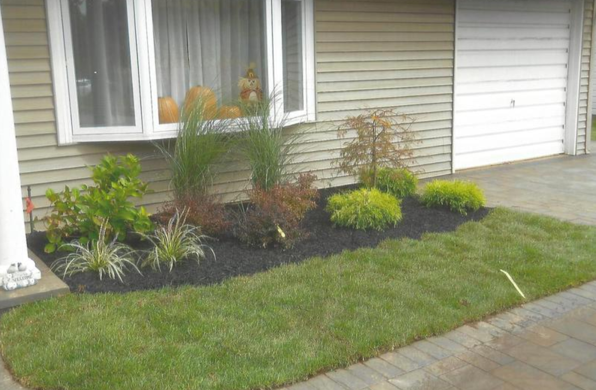 Front yard landscaping with green grass, mulch beds, and house with white window and garage.