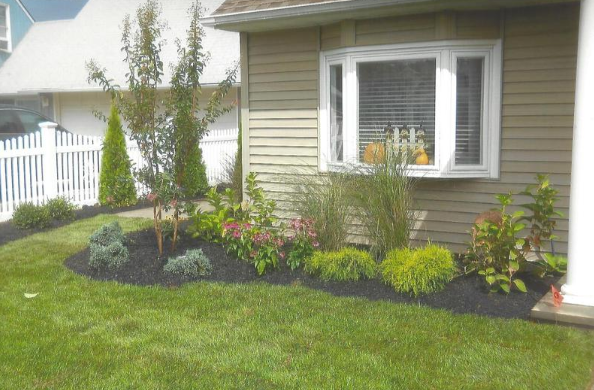 A landscaped front yard with a garden bed, green grass, and a bay window.