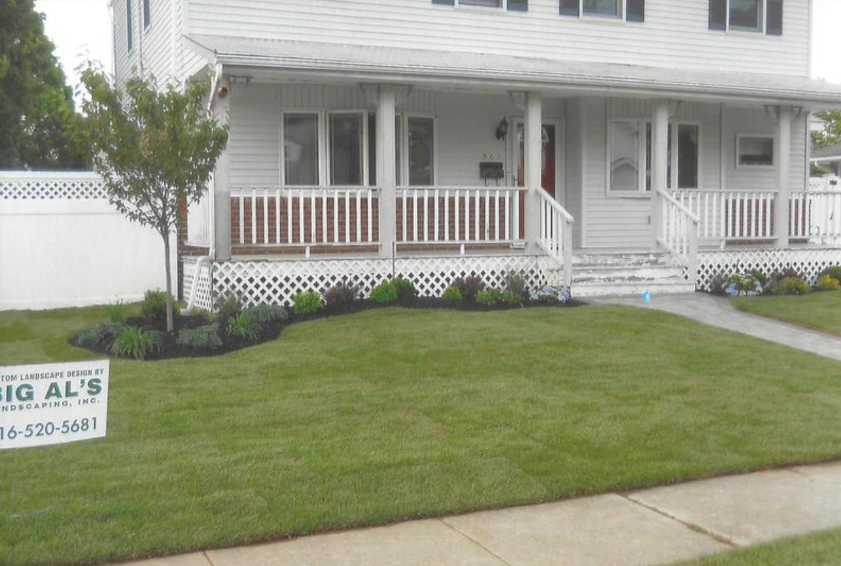 White house with porch and green lawn, landscaping, and tree; Big Al's sign in front.