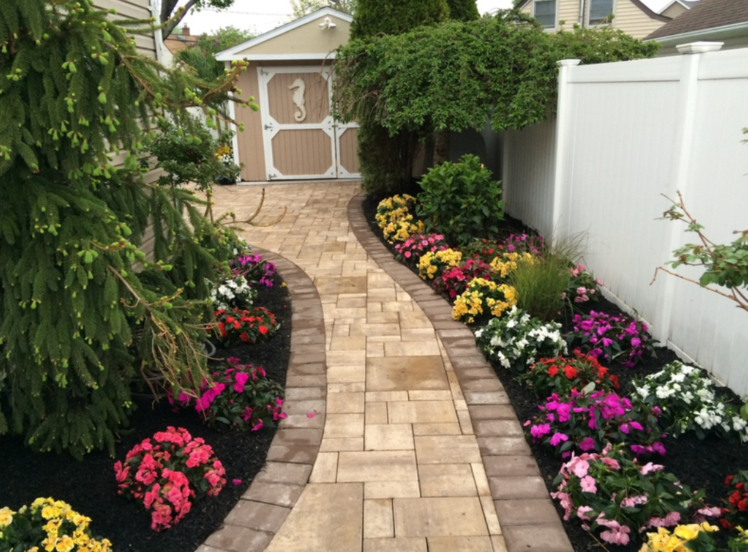 A stone path curves through a garden with flower beds. A shed is at the end.