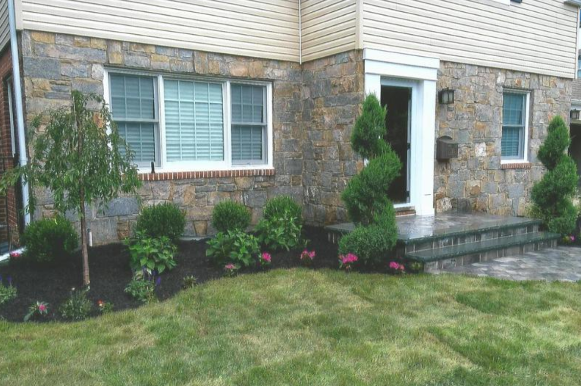House exterior with stone facade, green lawn, and landscaped flowerbeds.