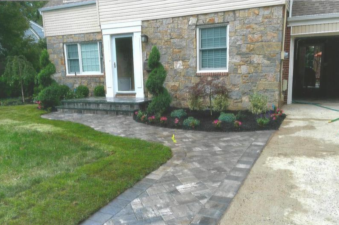 Stone house with landscaped front yard, paved walkway, and flower beds.