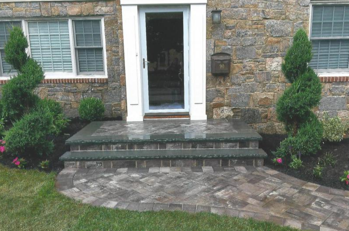 Stone steps and walkway leading to a front door with spiral topiary bushes and stone siding.