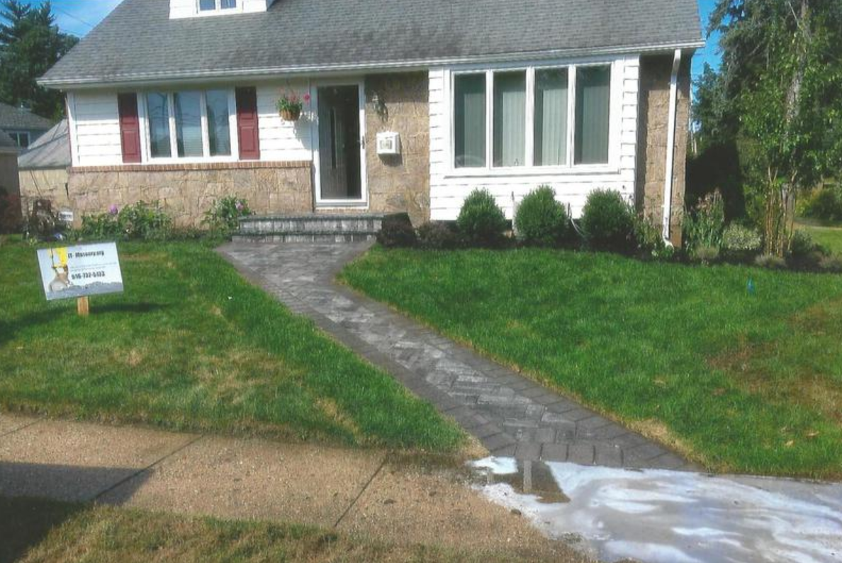 Brick walkway leads to a house with lawn. A sign and soapy water are in view.