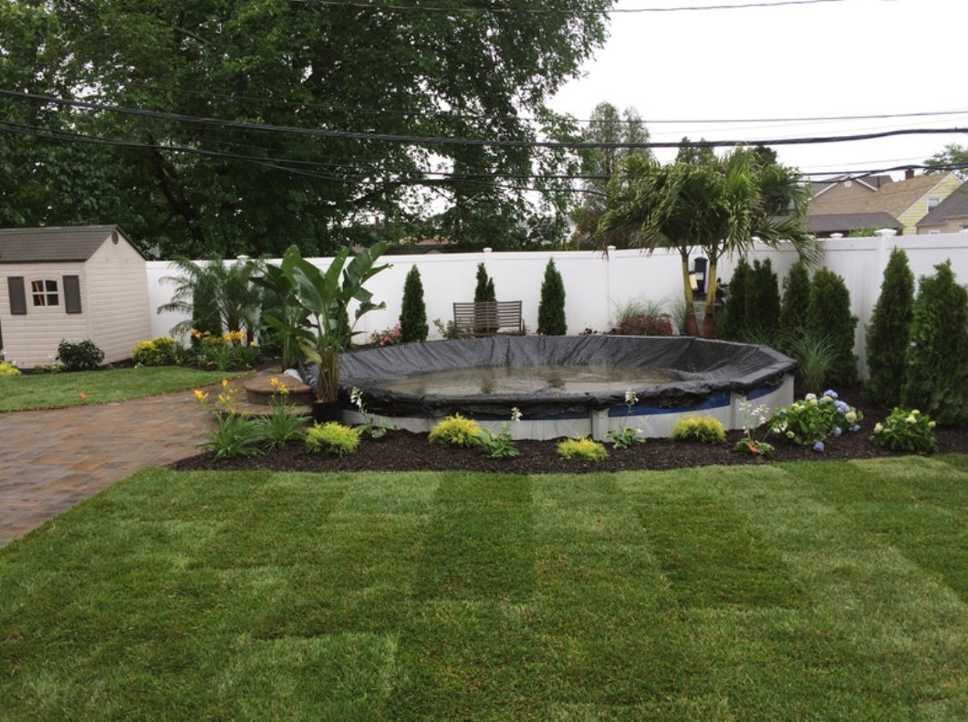 Backyard with covered above-ground pool surrounded by landscaping, lawn, shed, and white fence.