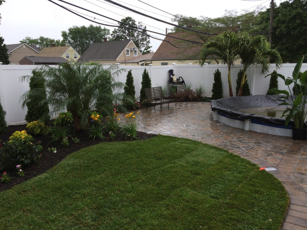 Backyard with lawn, pool, landscaping, white fence, and suburban houses in the background.