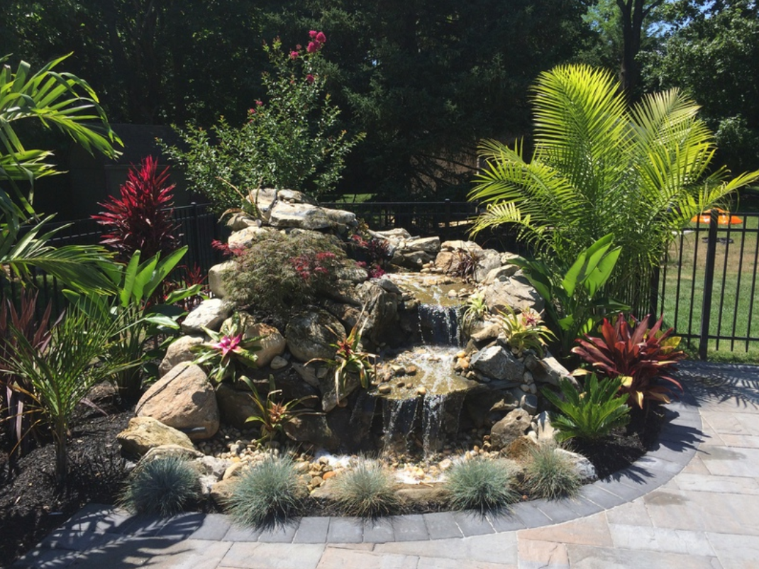 Waterfall feature in a garden, surrounded by lush greenery, with cascading water and stone.