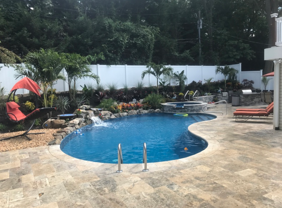 Pool with waterfall, landscaping, lounge chairs, and trees, surrounded by a stone patio.
