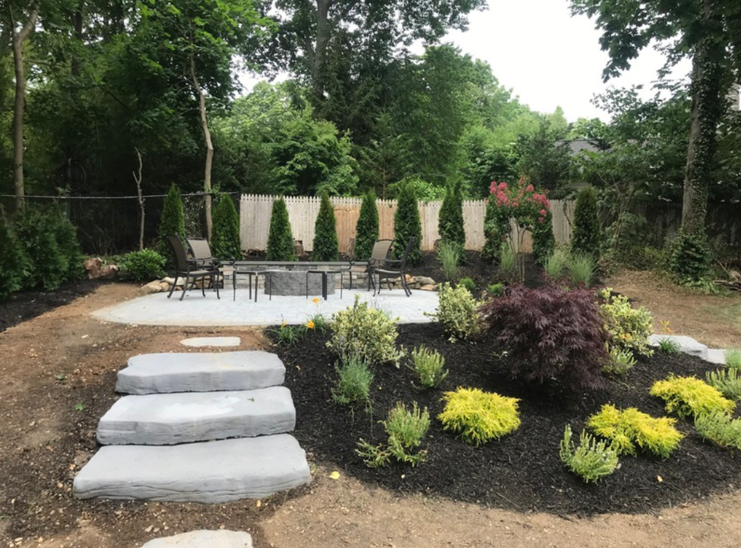 Stone steps lead to a patio with a fire pit and seating, surrounded by landscaping and trees.