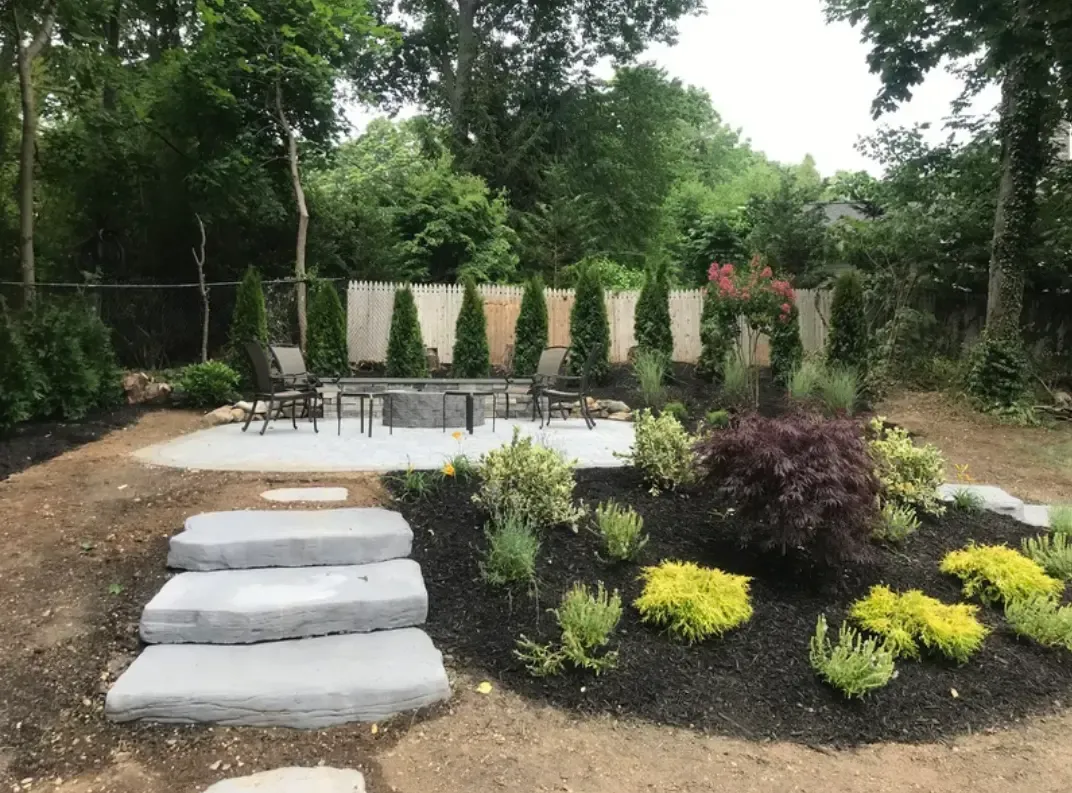 Backyard patio with stone steps, fire pit, seating, and landscaped garden.