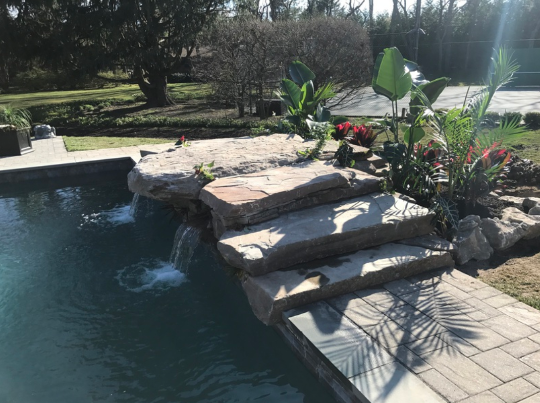 Stone steps lead into a pool with a waterfall feature, surrounded by greenery.