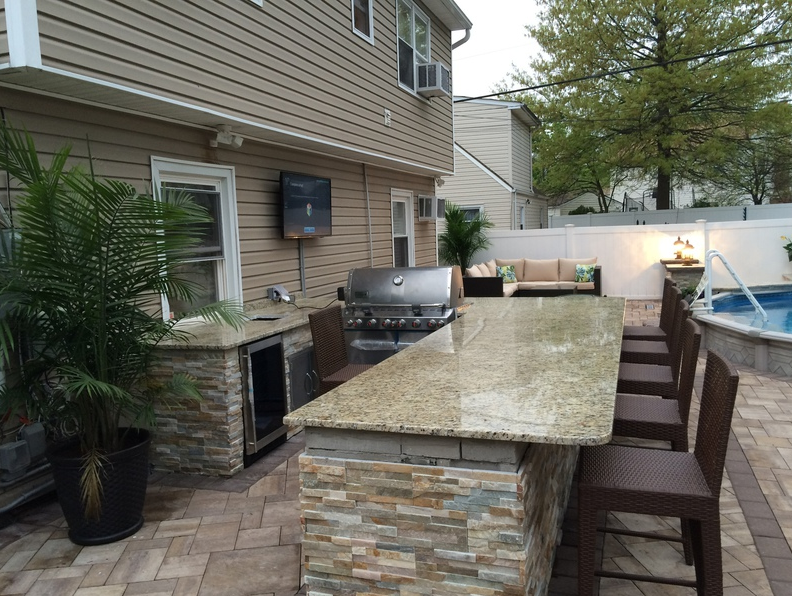 Outdoor kitchen with granite countertop, grill, bar seating, and pool.