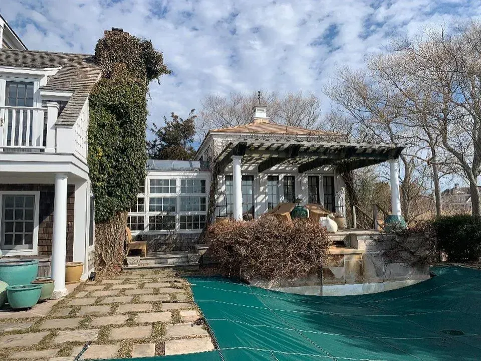 House with pool covered in green tarp, vines, and a pergola. Overcast sky.