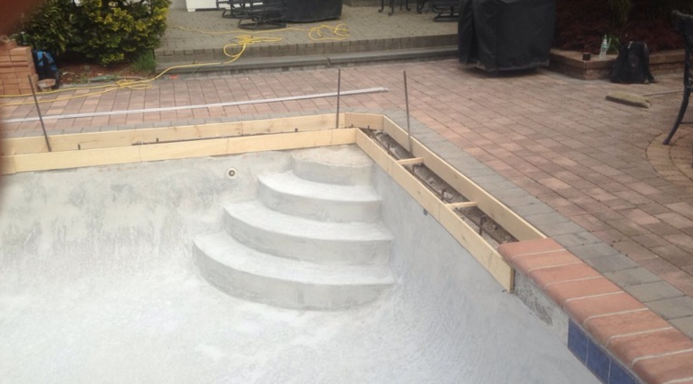 Concrete pool under construction with steps. Wooden forms and rebar are visible.