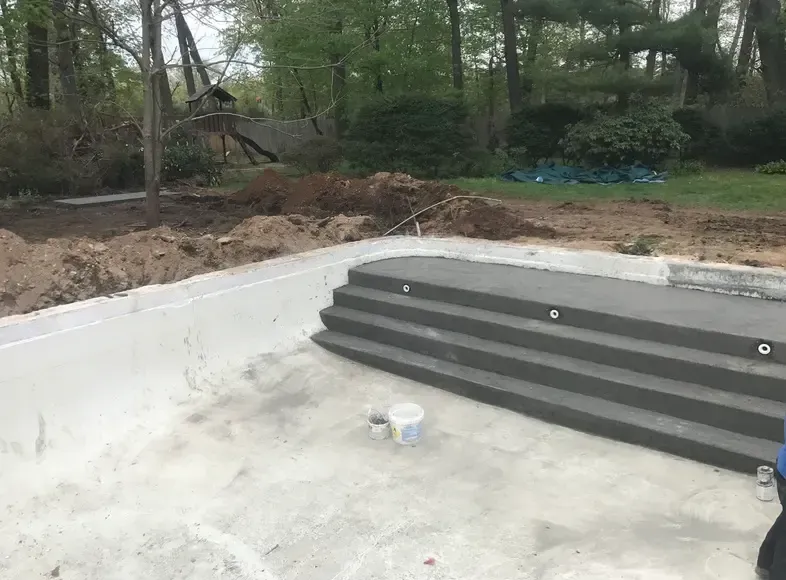 Concrete swimming pool under construction; gray steps, white surfaces; outdoor setting.