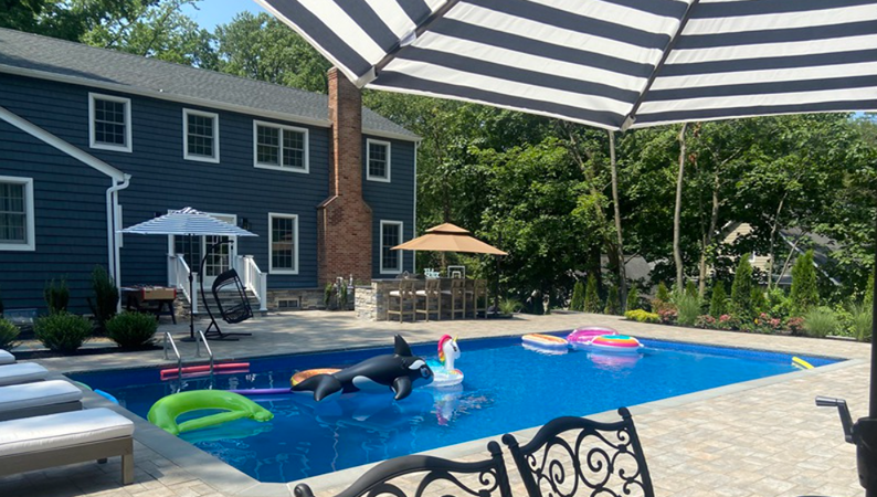 Backyard pool scene with a blue pool, floats, and a dark blue house.