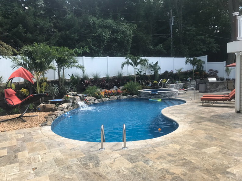 Backyard pool with waterfall, landscaping, lounge chairs, and a white fence.