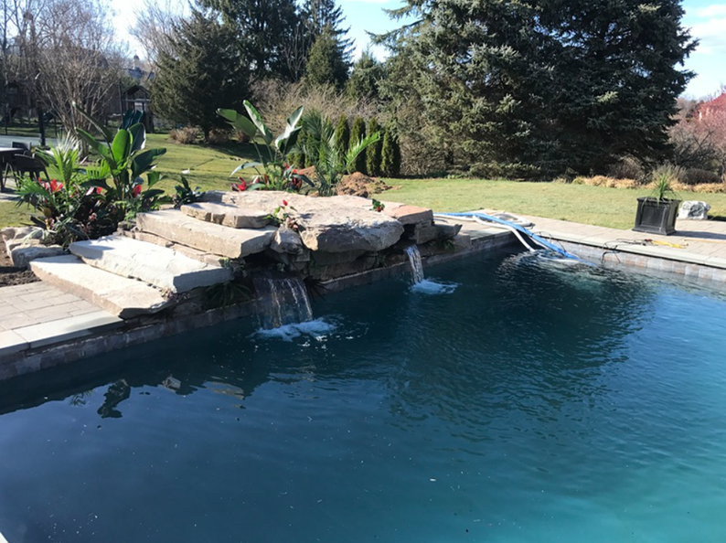 Pool with cascading waterfalls, surrounded by green grass and plants.