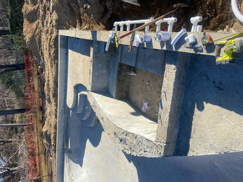 Concrete pool under construction with steps; tools and pipes nearby.
