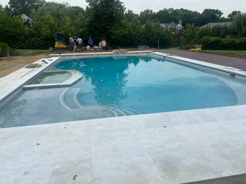 A rectangular swimming pool with a spa, filled with water. Construction workers in the background.
