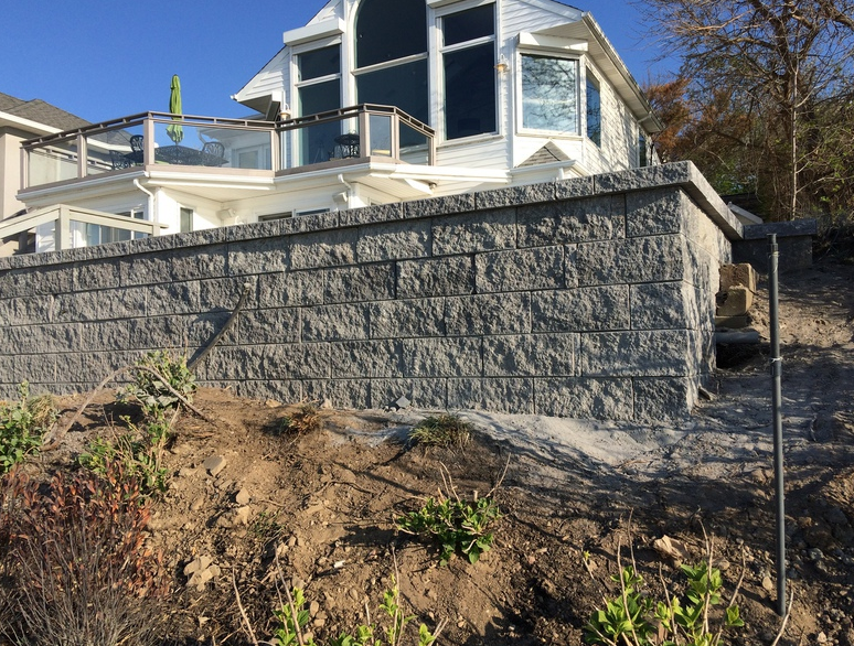 Gray stone retaining wall supporting a white house with a balcony.