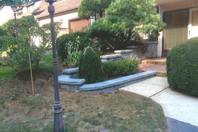 Landscaped front yard with stone retaining wall, manicured bushes, and a lamppost.