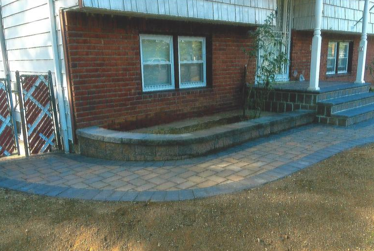 Brick house with brick patio, curved pathway, and steps leading to a porch.