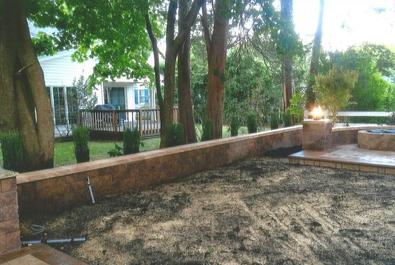 A low retaining wall with a sandy area in front, a house with a deck in the background.