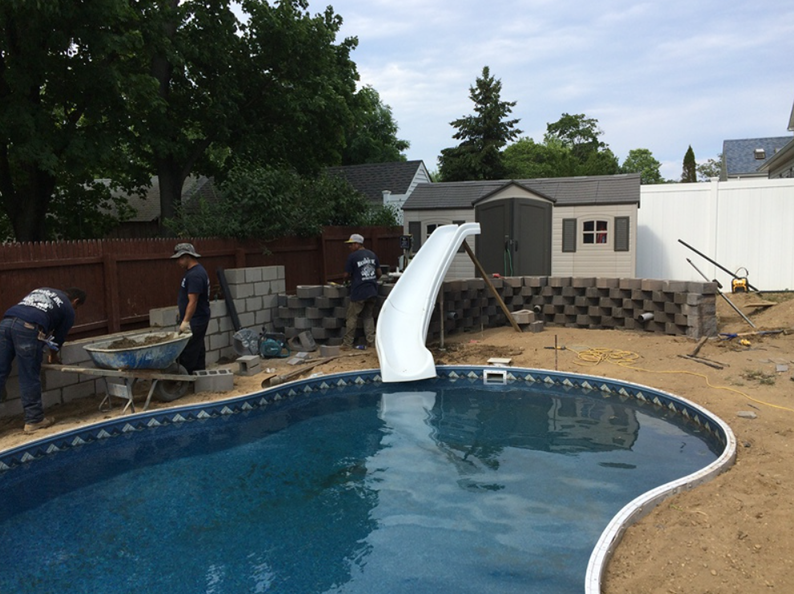 Construction of a pool with a slide. Workers build a retaining wall near a pool and shed.
