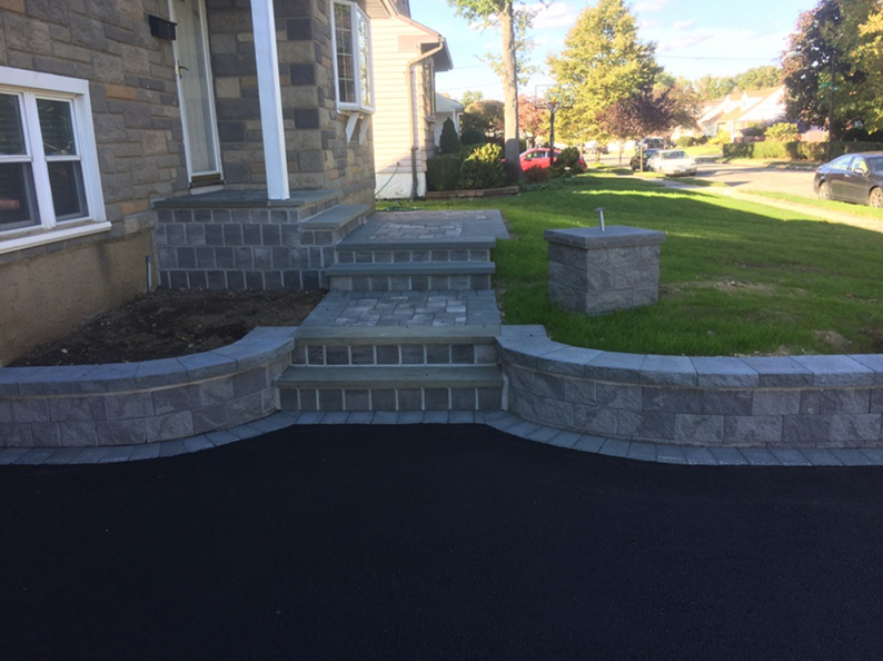 Stone steps leading to a house entrance, with a matching retaining wall and a lush green lawn.