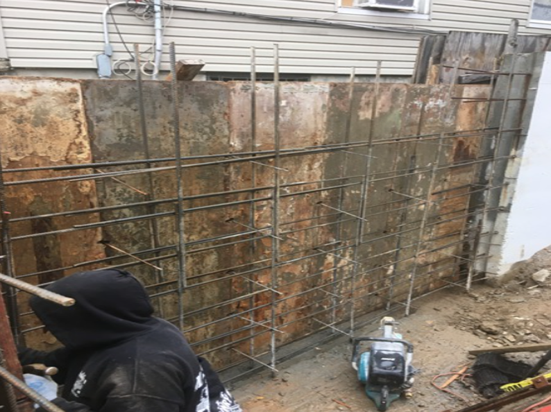 Construction site with a worker, metal rebar framework, and weathered wall panels.