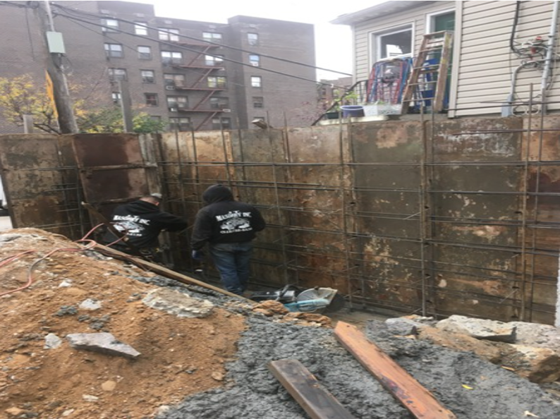 Construction workers building a retaining wall. Dirt, concrete, and metal forms are visible.
