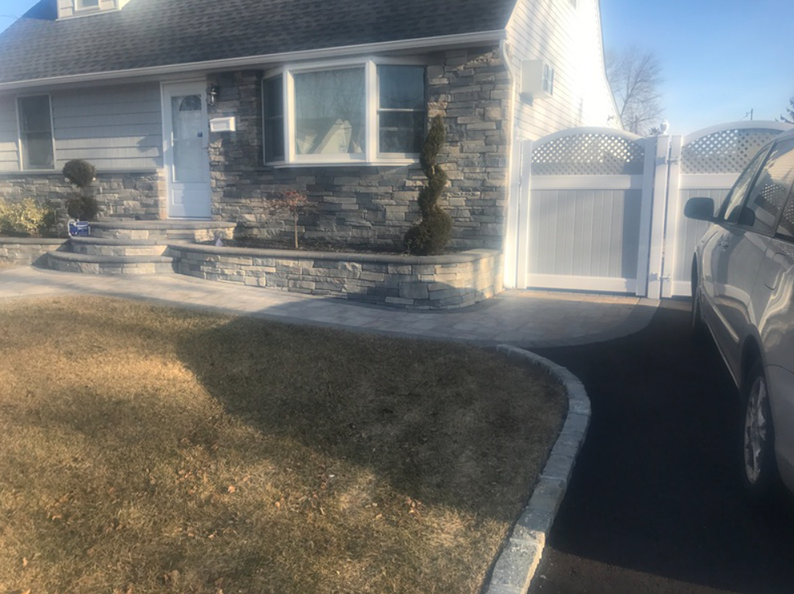 A house with gray stone facade, landscaped front yard, and paved driveway with a car.