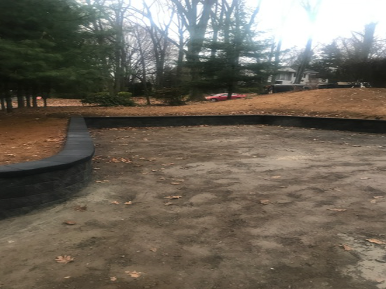 Gravel driveway bordered by a dark stone retaining wall, with trees and a house in the background.