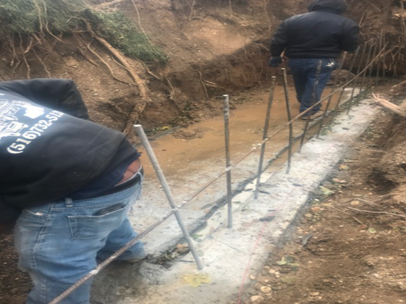 Two workers build a concrete wall outdoors, rebar placed in wet concrete.