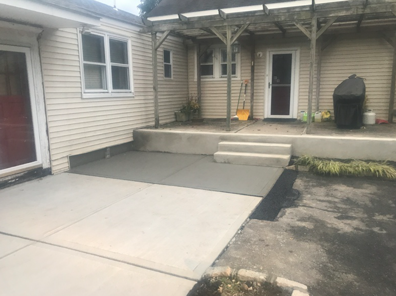 Newly poured concrete patio area with steps leading to a house entrance.
