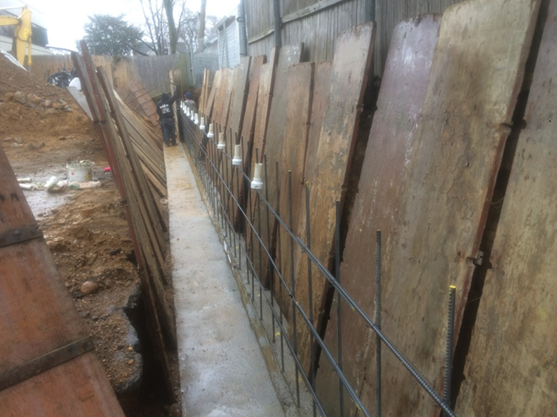 Construction site trench with wooden formwork, rebar, and concrete.