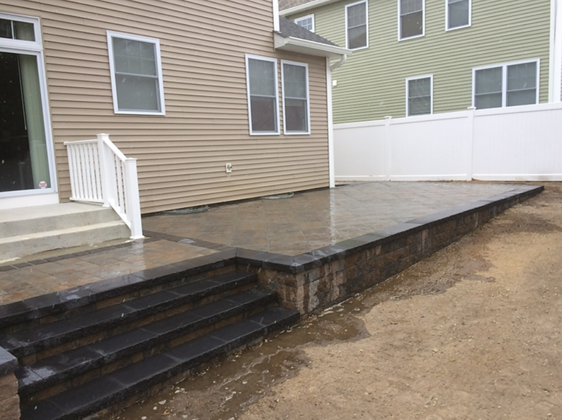 Patio with steps, retaining wall, house in background, wet pavers.