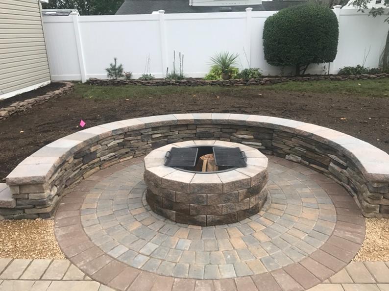 Circular stone fire pit with surrounding curved wall in a backyard.