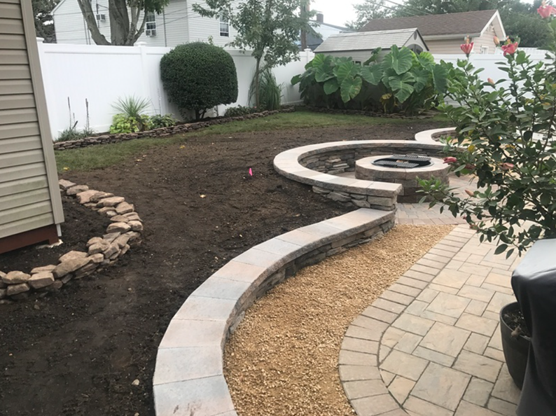 Backyard landscape with curved stone fire pit, pathway, and garden bed.