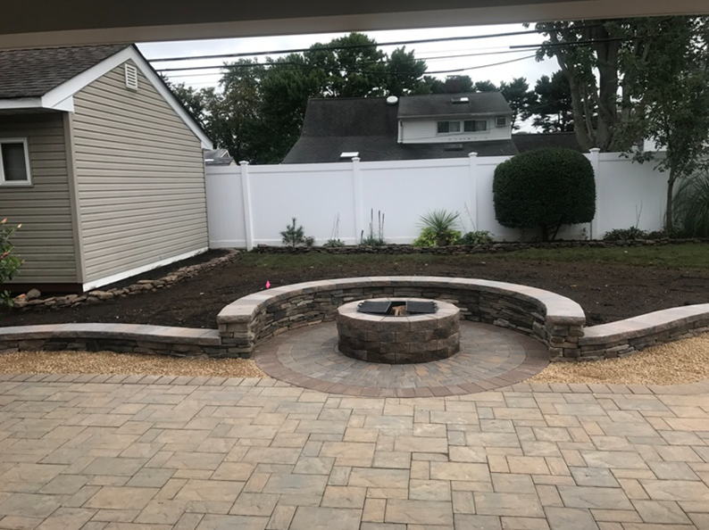 Backyard with a brick patio, stone fire pit, and retaining wall bordering a freshly mulched garden.