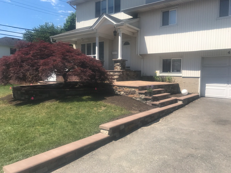 Beige two-story house with steps leading to the front door. A Japanese maple tree and retaining walls are in front.