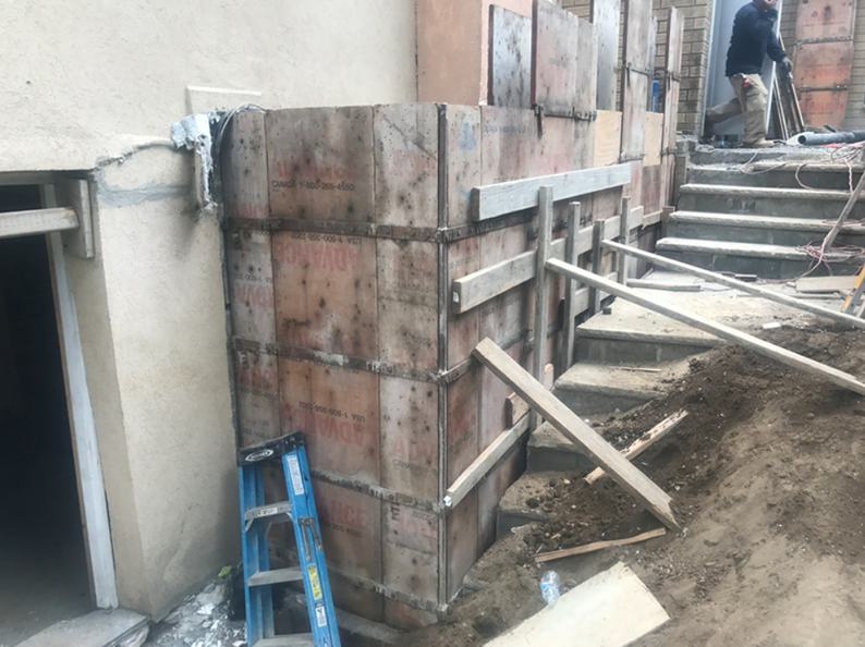 Construction site: Wooden forms for a retaining wall next to stairs and building entrance.