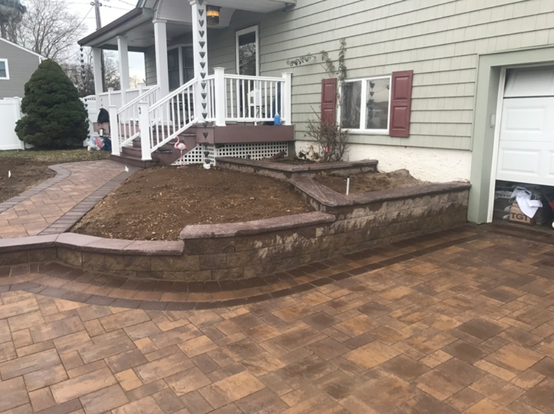 Brick patio and retaining walls lead to house entrance with steps.